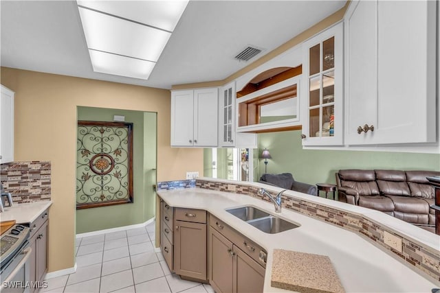 kitchen with white cabinets, sink, decorative backsplash, light tile patterned floors, and stainless steel range