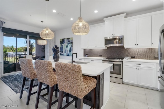 kitchen featuring stainless steel appliances, sink, decorative light fixtures, white cabinetry, and an island with sink