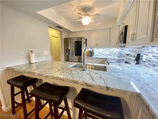 kitchen featuring appliances with stainless steel finishes, a kitchen bar, kitchen peninsula, and sink