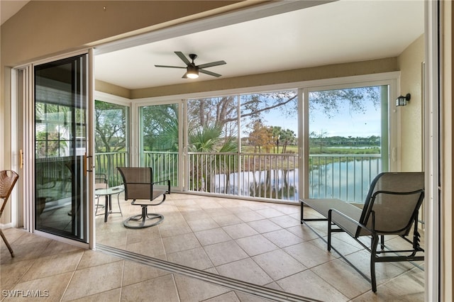 sunroom with ceiling fan and a water view