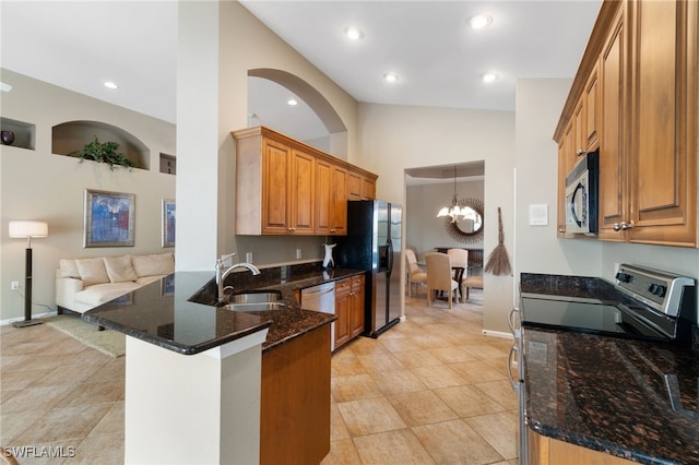 kitchen with kitchen peninsula, stainless steel appliances, sink, a notable chandelier, and dark stone countertops