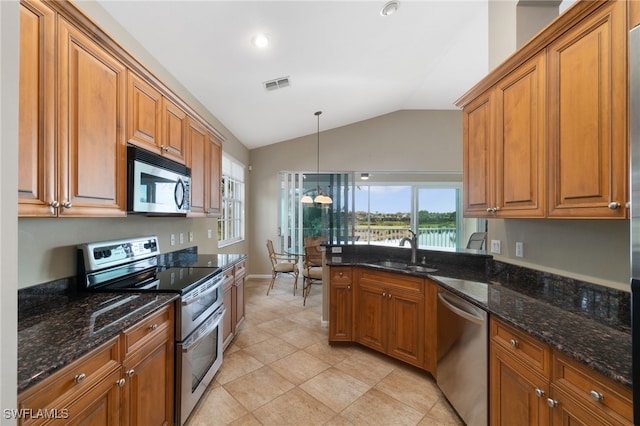 kitchen with pendant lighting, lofted ceiling, dark stone counters, sink, and stainless steel appliances