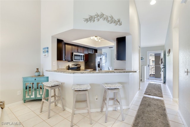 kitchen with a breakfast bar, light tile patterned floors, stainless steel appliances, and kitchen peninsula