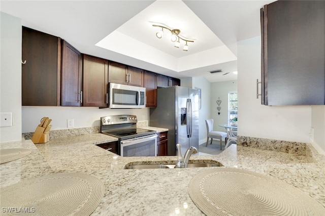 kitchen featuring light stone counters, a raised ceiling, sink, and appliances with stainless steel finishes