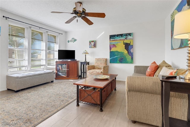 living room with a textured ceiling, light wood-type flooring, and ceiling fan