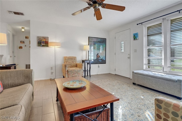 living area featuring a textured ceiling, ceiling fan, visible vents, and baseboards