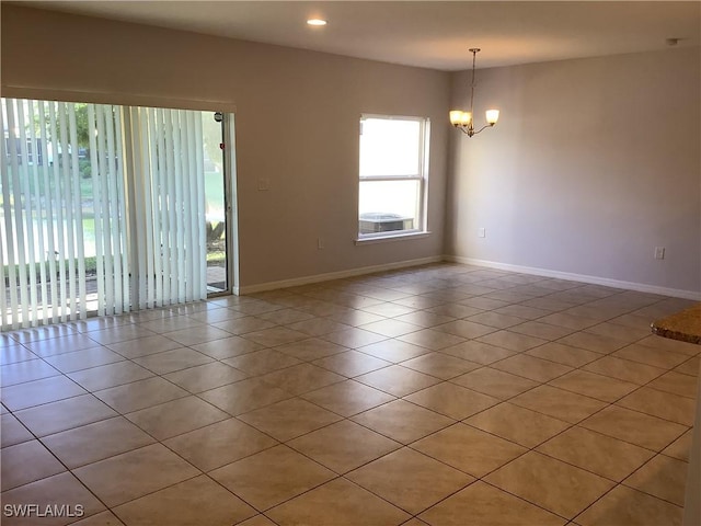 tiled spare room featuring an inviting chandelier