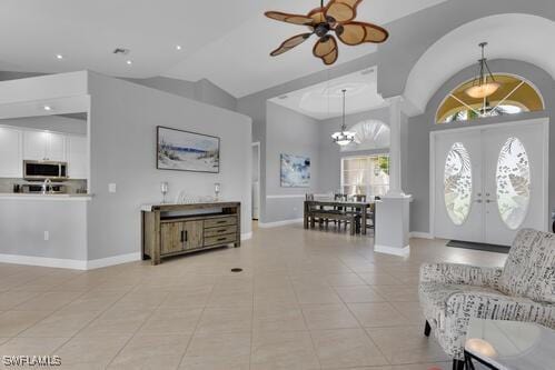 tiled foyer featuring ceiling fan with notable chandelier, high vaulted ceiling, and french doors