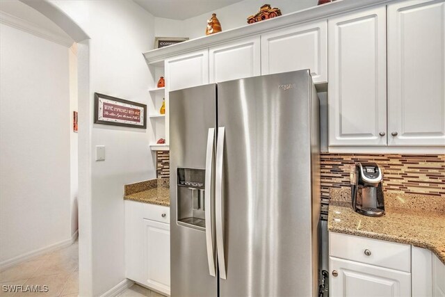 kitchen with light stone counters, arched walkways, tasteful backsplash, white cabinets, and stainless steel fridge with ice dispenser