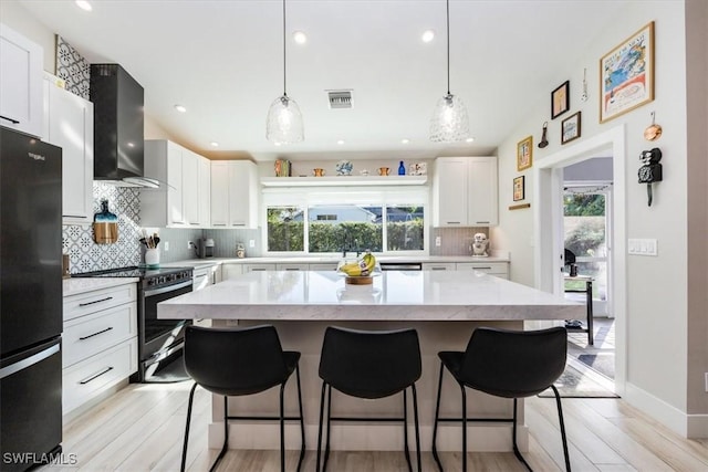 kitchen with stainless steel electric stove, wall chimney exhaust hood, a wealth of natural light, and fridge