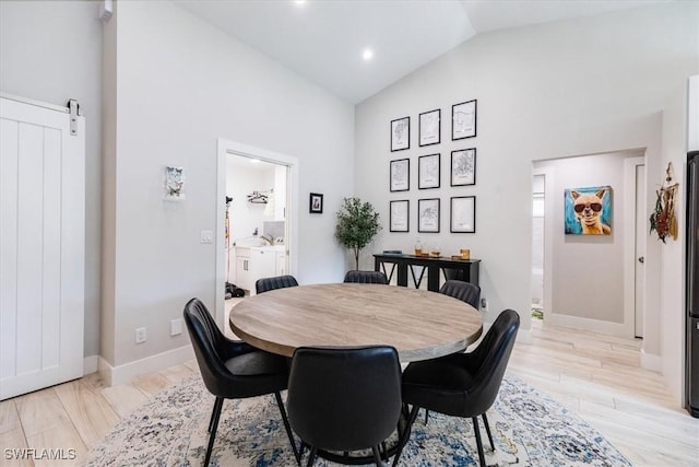 dining area featuring a barn door, light hardwood / wood-style floors, and high vaulted ceiling