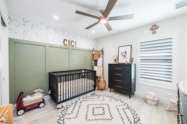 bedroom featuring a crib, light wood-type flooring, and ceiling fan