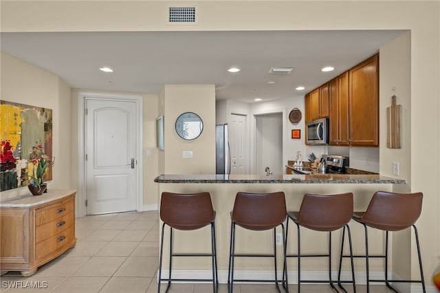 kitchen with a kitchen breakfast bar, light tile patterned flooring, dark stone countertops, and appliances with stainless steel finishes