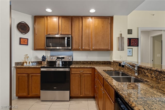 kitchen featuring sink, light tile patterned floors, dark stone counters, and appliances with stainless steel finishes