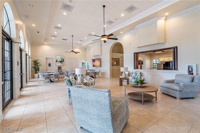 tiled living room with a high ceiling, a tray ceiling, ceiling fan, and ornamental molding