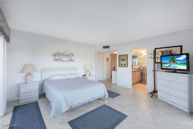 bedroom with light tile patterned flooring, a textured ceiling, and connected bathroom