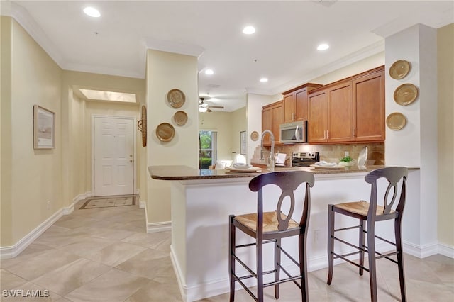 kitchen featuring a kitchen bar, decorative backsplash, brown cabinets, appliances with stainless steel finishes, and a peninsula