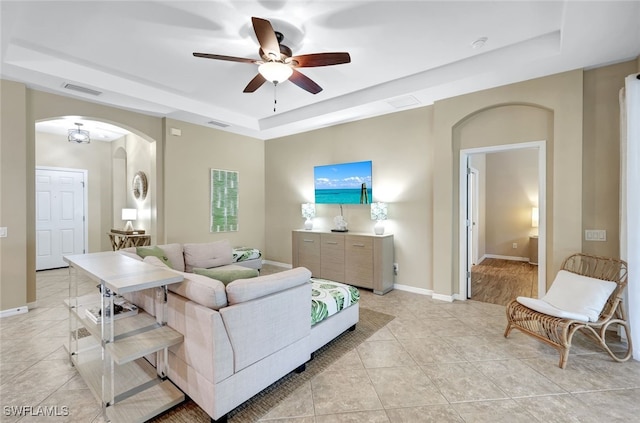 tiled living room with a tray ceiling and ceiling fan