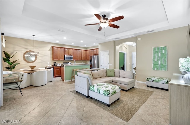 living room with a tray ceiling, ceiling fan, and light tile patterned flooring