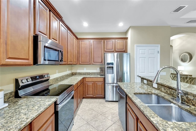 kitchen with appliances with stainless steel finishes, light tile patterned floors, light stone counters, and sink