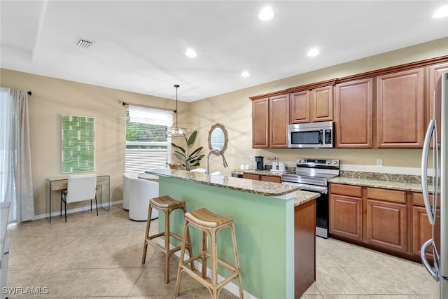 kitchen featuring stainless steel appliances, an inviting chandelier, light stone counters, pendant lighting, and a center island with sink