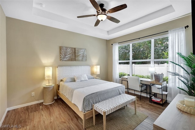 bedroom with hardwood / wood-style flooring, ceiling fan, and a tray ceiling