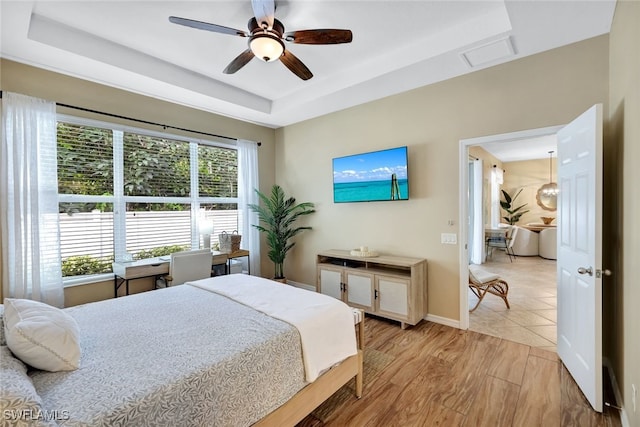 bedroom featuring ceiling fan, light hardwood / wood-style floors, and a raised ceiling