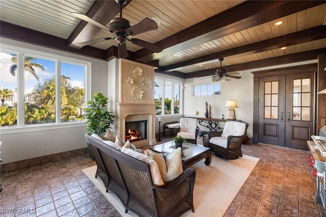 living area featuring a warm lit fireplace, baseboards, beam ceiling, and french doors