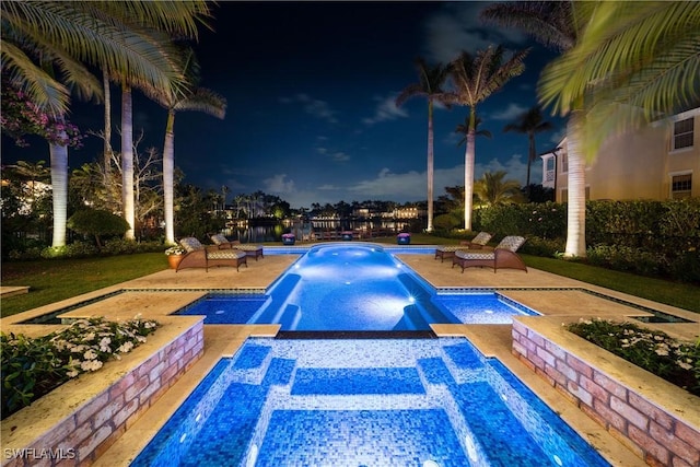 pool at night with a pool with connected hot tub and a patio