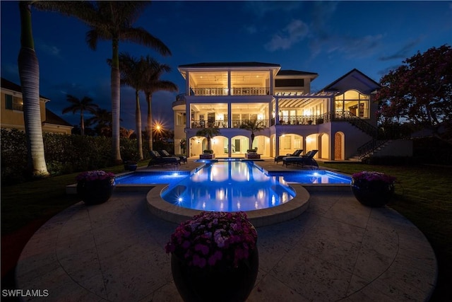 pool at night featuring a pool with connected hot tub, stairway, and a patio