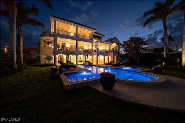 pool at night with a patio area, an outdoor pool, a lawn, and an in ground hot tub