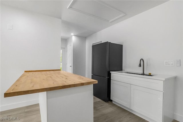 kitchen featuring wood counters, black fridge, sink, white cabinets, and light hardwood / wood-style floors