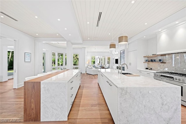 kitchen featuring light wood-type flooring, sink, stainless steel stove, white cabinetry, and a large island