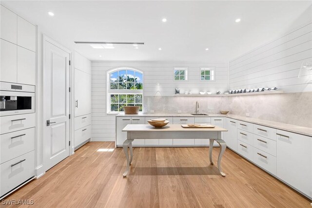 kitchen featuring white oven, sink, white cabinets, and light hardwood / wood-style floors