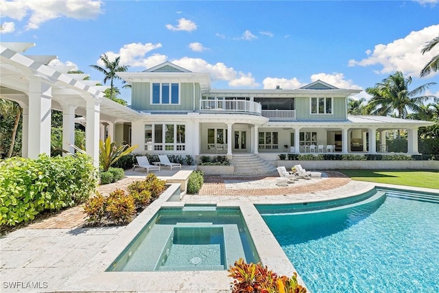 back of house with a swimming pool with hot tub, a balcony, a pergola, and a patio