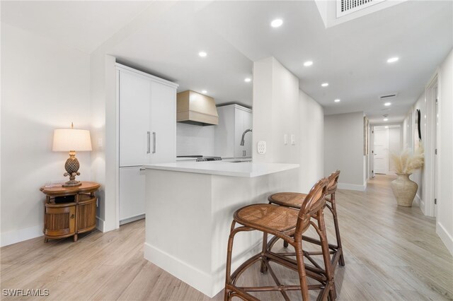 kitchen with custom exhaust hood, white cabinets, sink, light wood-type flooring, and kitchen peninsula