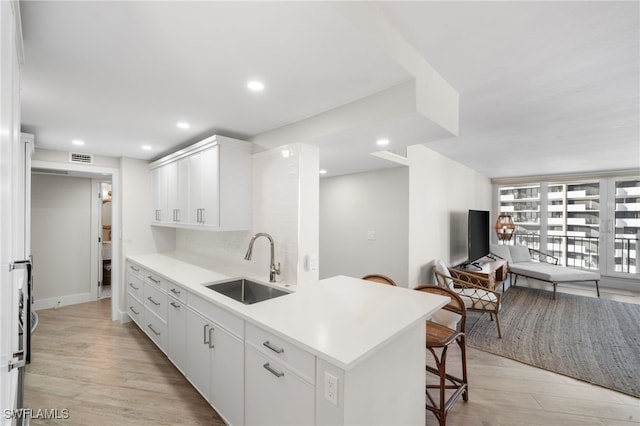 kitchen with tasteful backsplash, sink, white cabinets, and light wood-type flooring