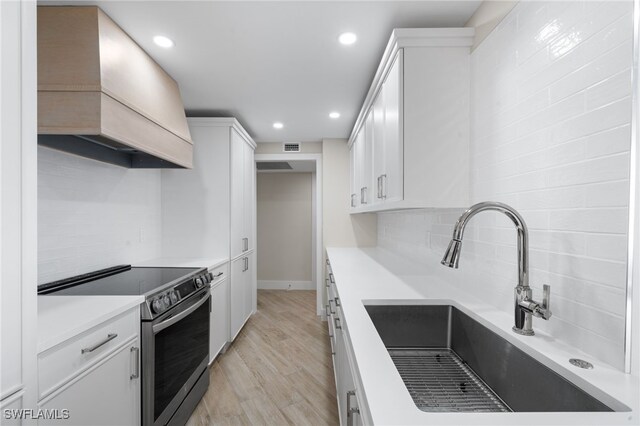 kitchen featuring stainless steel electric range, custom exhaust hood, sink, light hardwood / wood-style floors, and white cabinetry