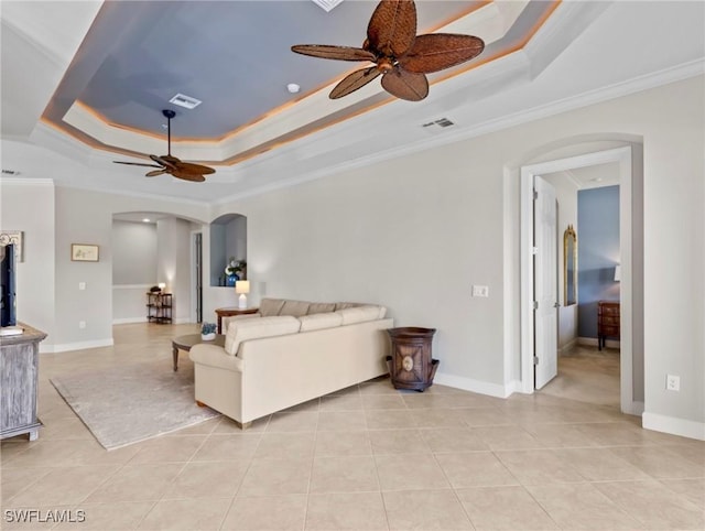 living room with a tray ceiling, ceiling fan, light tile patterned floors, and ornamental molding