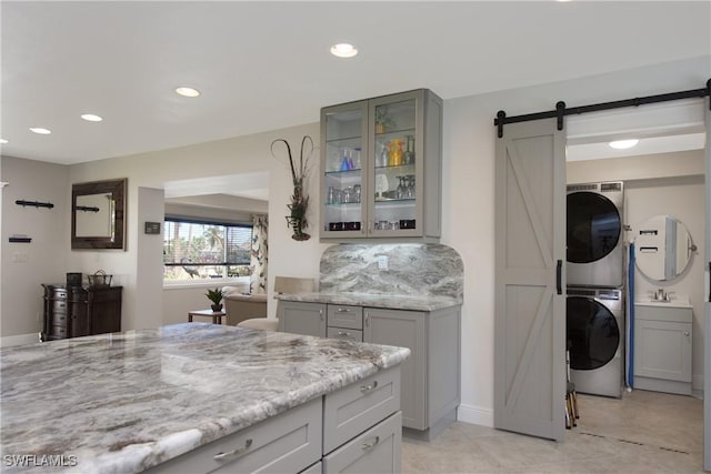 kitchen featuring light stone countertops, backsplash, a barn door, stacked washer / dryer, and gray cabinets