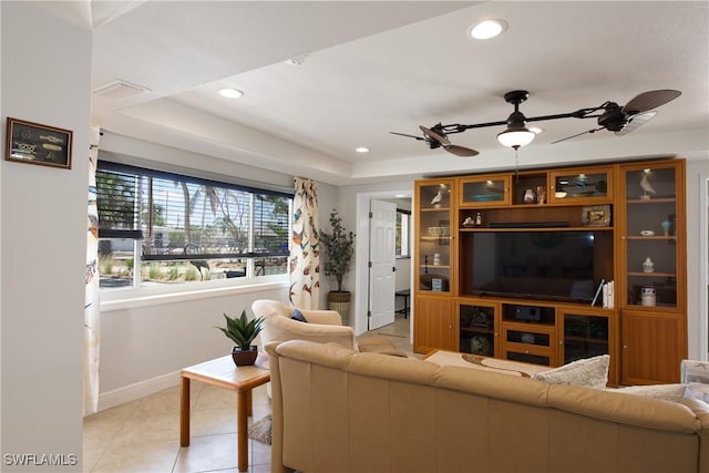 tiled living room with ceiling fan and a tray ceiling