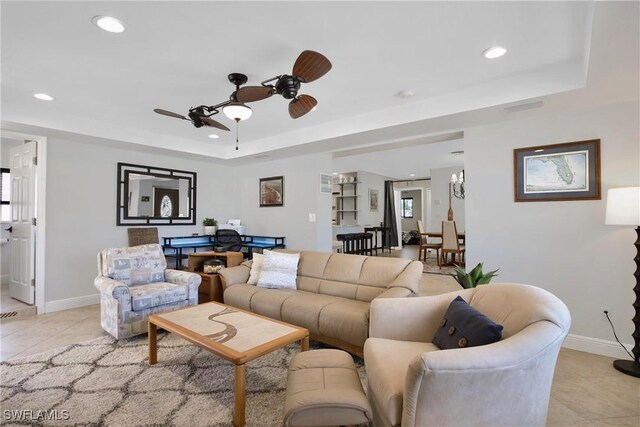 living room featuring a raised ceiling, ceiling fan, and light tile patterned flooring