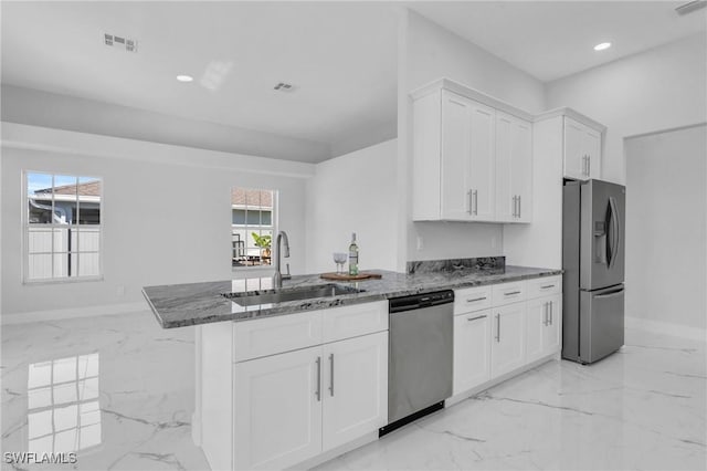 kitchen with kitchen peninsula, dark stone counters, stainless steel appliances, sink, and white cabinets