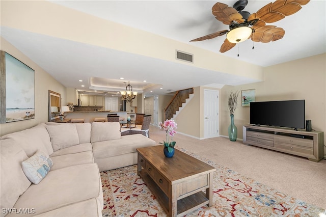 carpeted living room with a raised ceiling and ceiling fan with notable chandelier