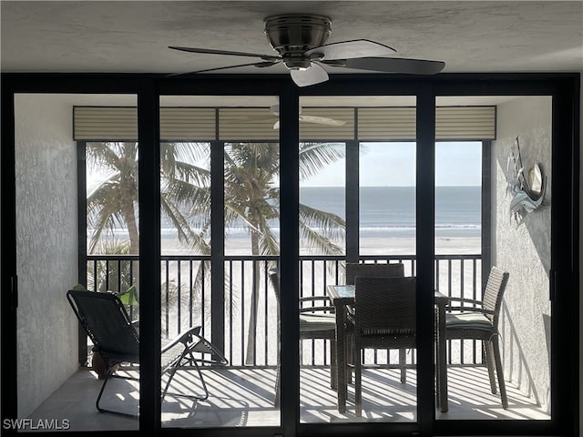 sunroom featuring a view of the beach, a water view, and ceiling fan