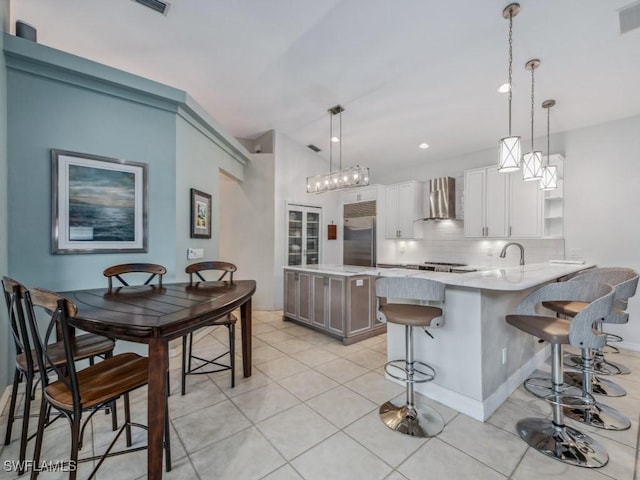 kitchen featuring hanging light fixtures, decorative backsplash, wall chimney exhaust hood, and stainless steel built in refrigerator