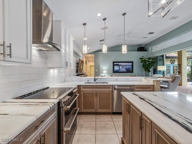 kitchen with sink, decorative light fixtures, wall chimney range hood, stainless steel appliances, and white cabinets