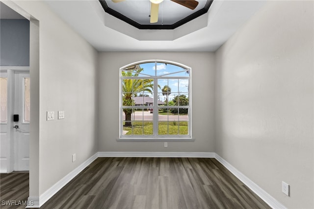 empty room featuring a tray ceiling, crown molding, ceiling fan, and dark wood-type flooring