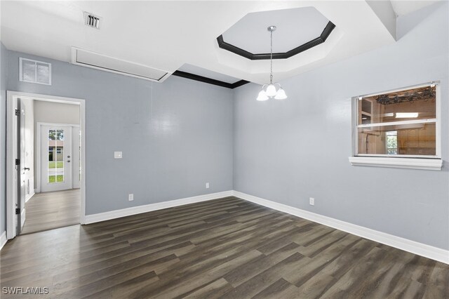 empty room featuring a raised ceiling, dark wood-type flooring, and a notable chandelier