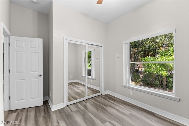 unfurnished bedroom featuring multiple windows, light wood-type flooring, a closet, and ceiling fan